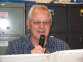 Tom Yackish holding a microphone, reading from a white binder